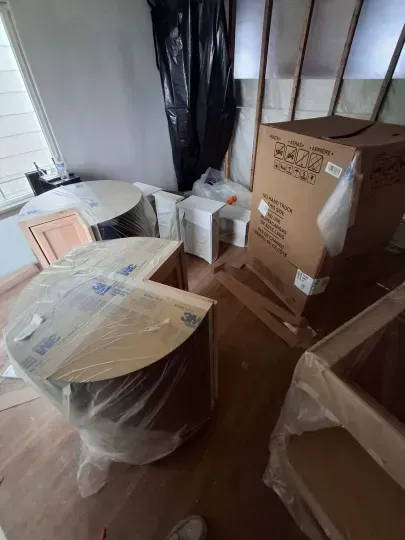 Packed moving boxes and wrapped furniture in a small room with wood flooring.