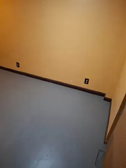 Empty room with yellow walls, gray floor, and electrical outlets along the baseboard