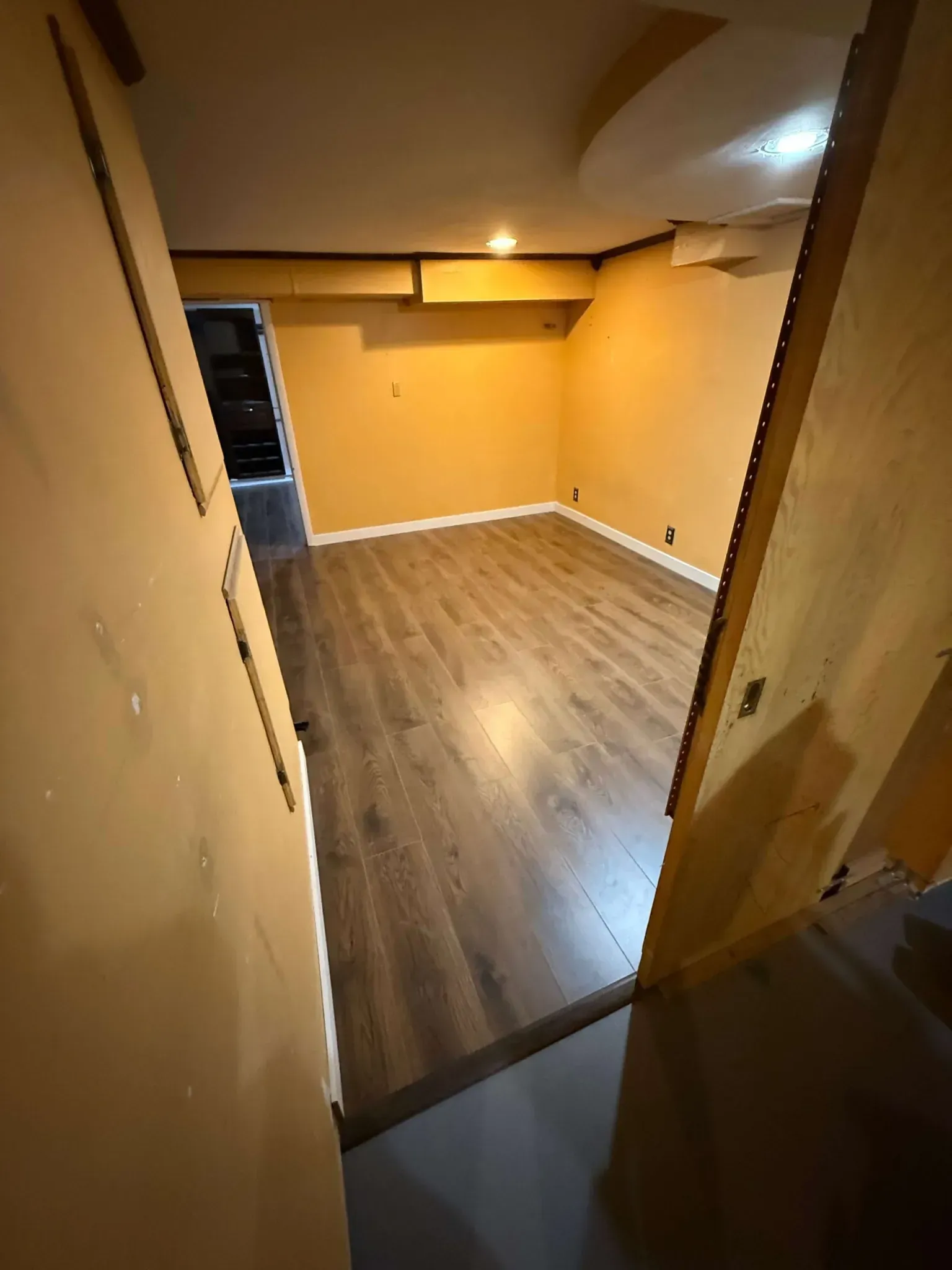 Empty unfurnished room with wood flooring, beige walls, and a doorway in the foreground