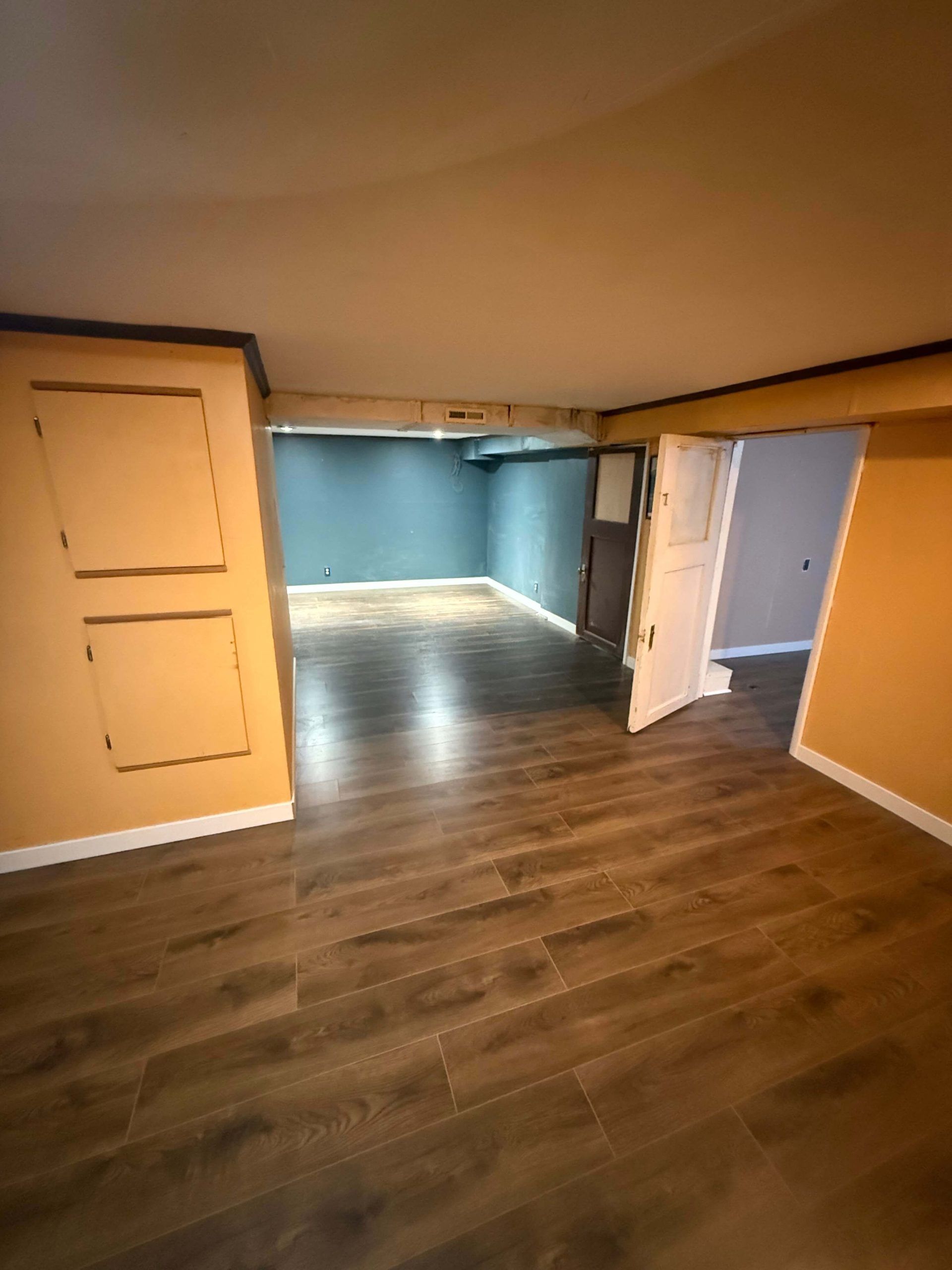 Empty room with wood-look flooring, orange walls, and a blue-walled adjacent area through open doorways.