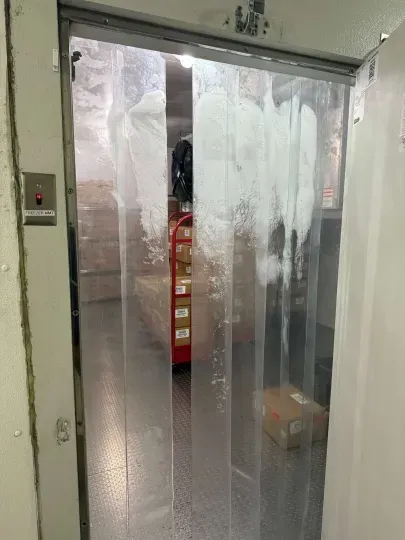 Open industrial doorway with clear strip curtains and a red pallet jack visible inside