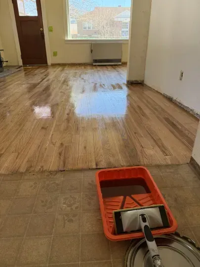 Freshly cleaned hardwood floor with a mop and red bucket in the foreground