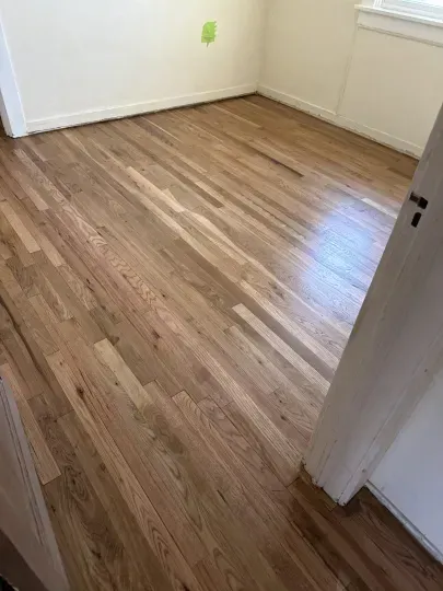 Empty room with light wood flooring and white walls, viewed from an open doorway.