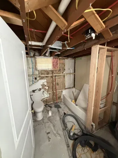 Unfinished bathroom under renovation with exposed studs, toilet, debris, and a large pipe on the floor