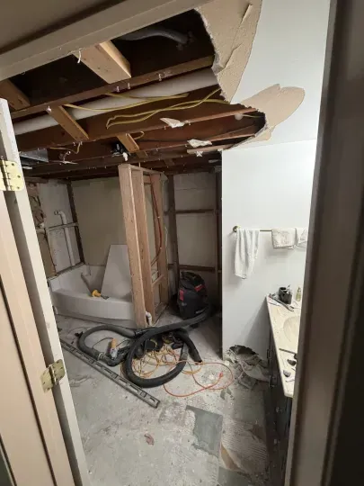 Damaged room with collapsed ceiling, exposed beams, debris, and tools on the floor