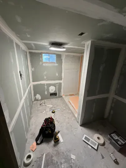 Small unfinished drywall room with construction tools and materials scattered on the floor.