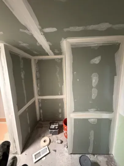 Unfinished drywall room with taped seams, white trim, and tools scattered on the floor.