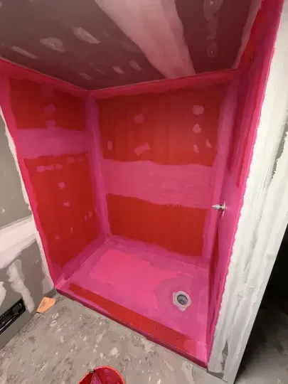 Red-painted shower stall with unfinished walls and a drain on the floor