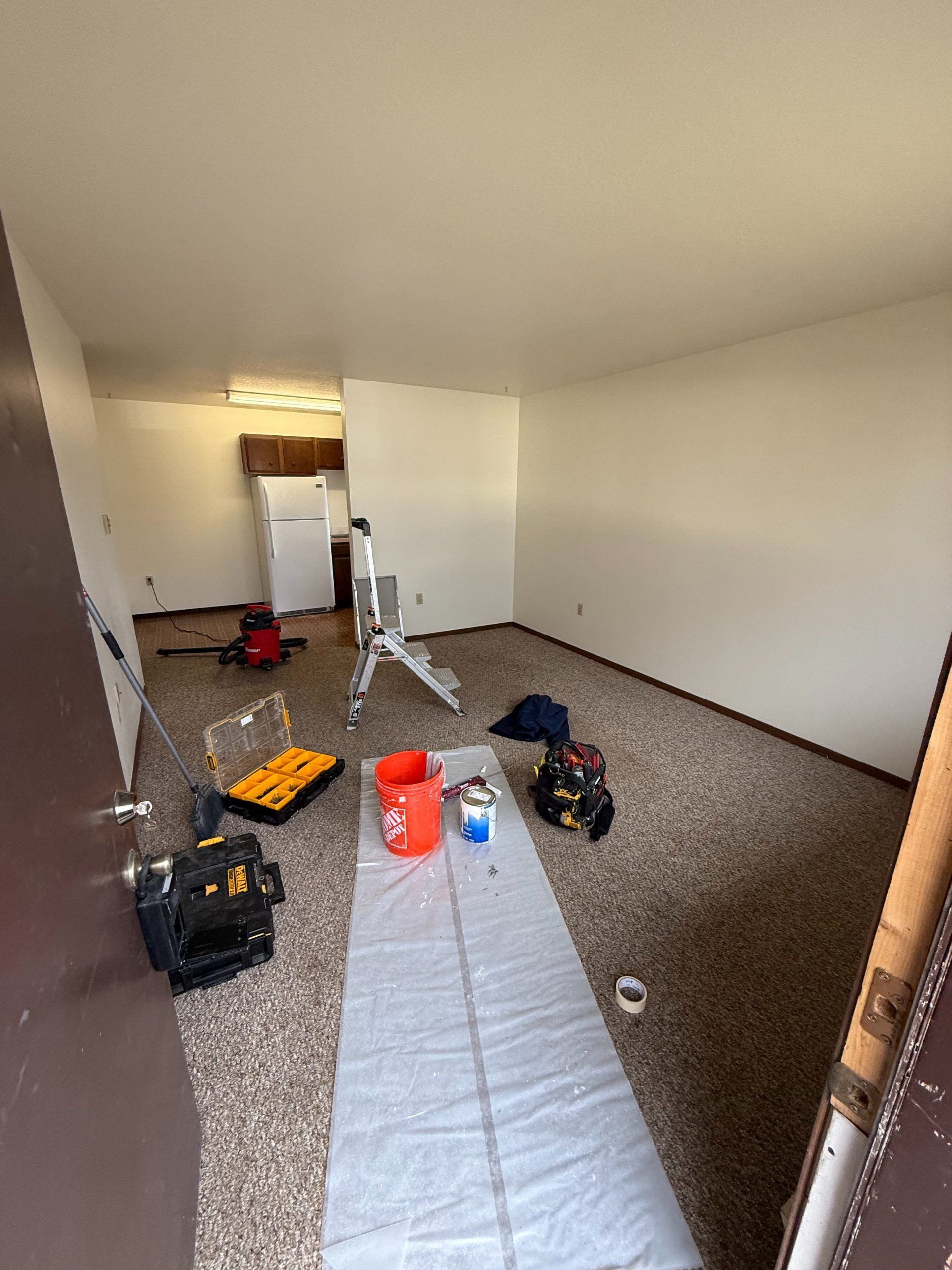 Empty room with carpet and scattered tools, buckets, and supplies near a doorway.