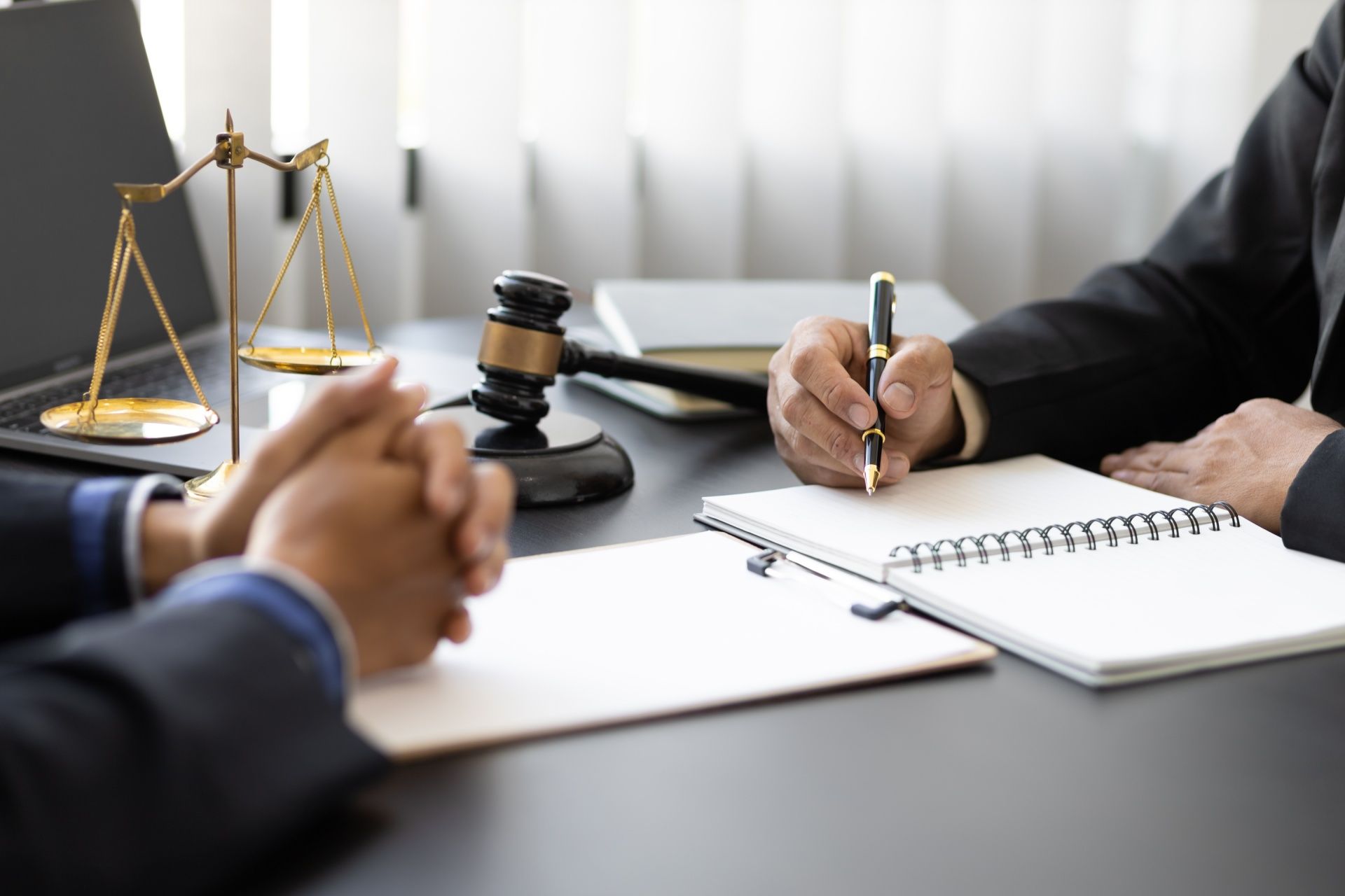 A lawyer is sitting at a desk with a client and writing in a notebook.