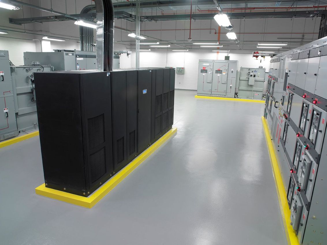 Data center aisle with black server racks and white cabinets on a gray floor with yellow safety borders