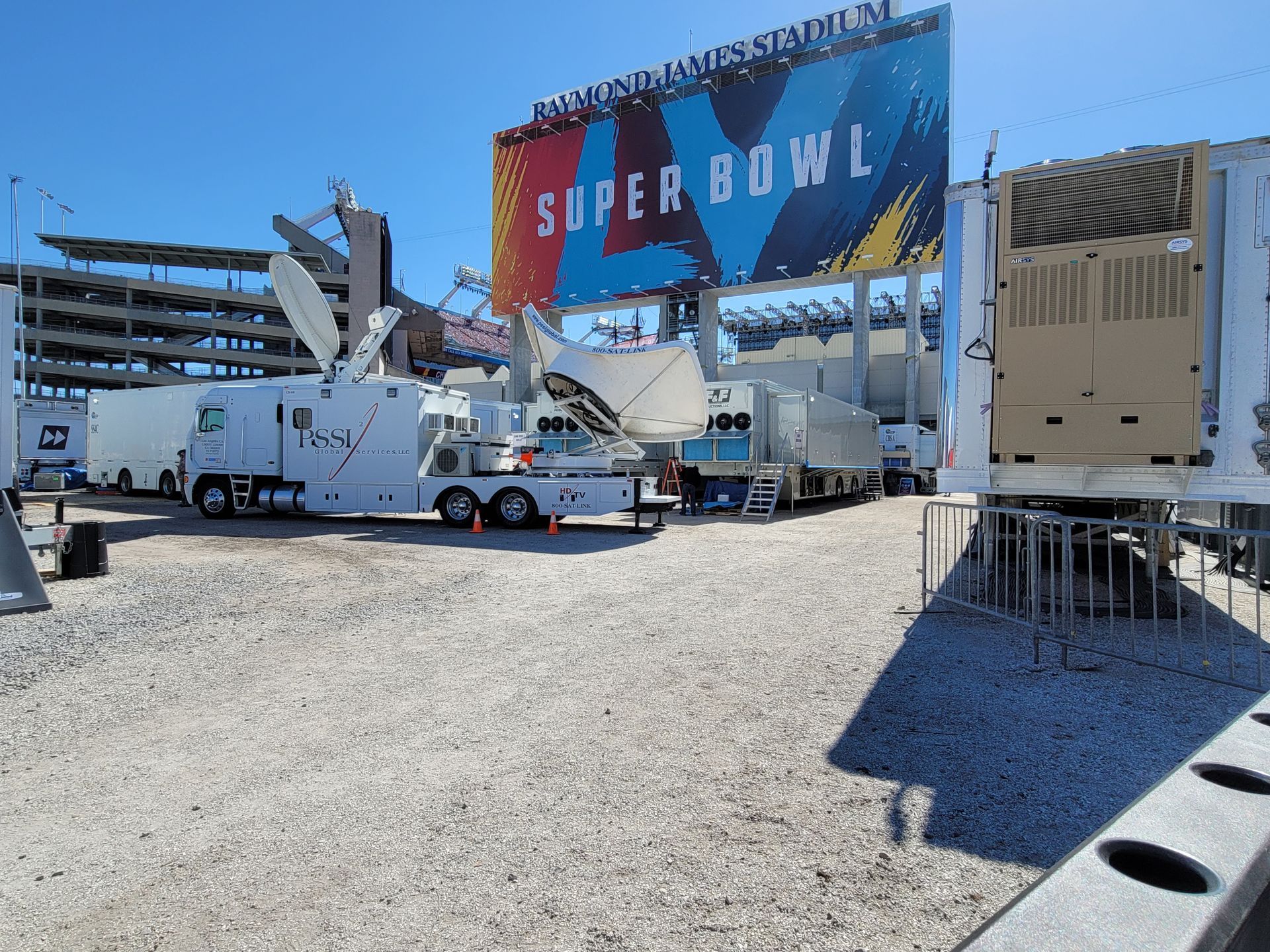 Super Bowl outdoor setup with trucks, cranes, and a large colorful billboard under construction