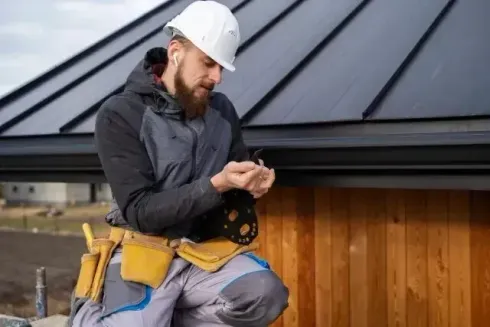Chimney Sweep Portland - A construction worker is sitting on the roof looking at his phone.