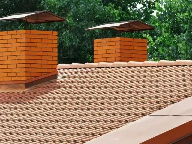 Chimney-Sweep-Portland - Two brick chimneys with protective caps rise above a tan tiled roof.
