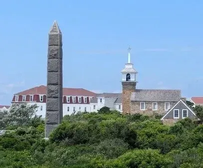 Chimney-Sweep-Portland-A tall stone obelisk stands in front of a stone church with a steeple and bell tower, and a large white building with a red roof.