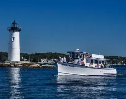 Chimney-Sweep-Portland-White lighthouse stands on a rocky shore as a passenger boat named
