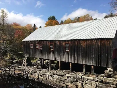 Chimney-Sweep-Portland-A rustic wooden covered bridge extends over a rocky riverbank, surrounded by vibrant autumn foliage under a partly cloudy blue sky, evoking tranquility and nostalgia.