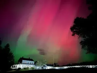 Chimney-Sweep-Portland-A vibrant aurora borealis illuminates the night sky with pink and green hues above a building and silhouetted trees.
