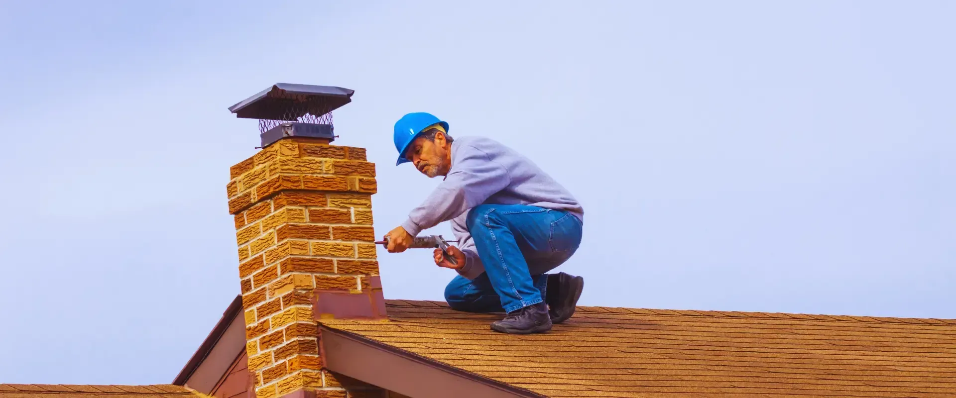 A man is kneeling on top of a roof fixing a chimney.