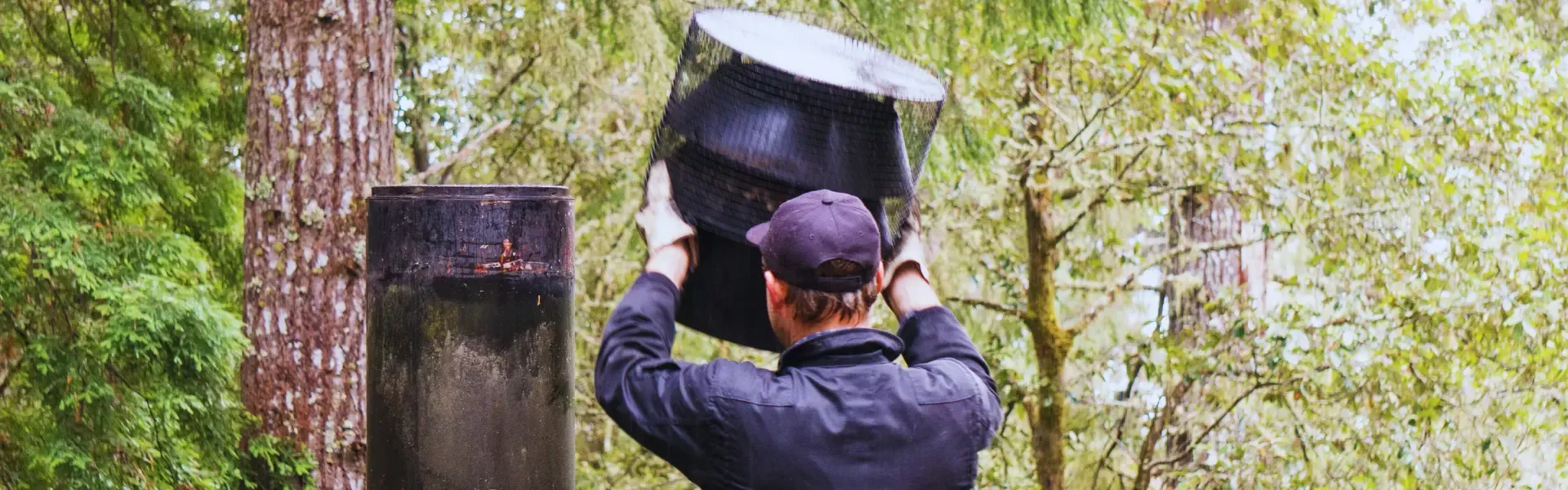 A man is holding a large black object in his hands while standing next to a tree.