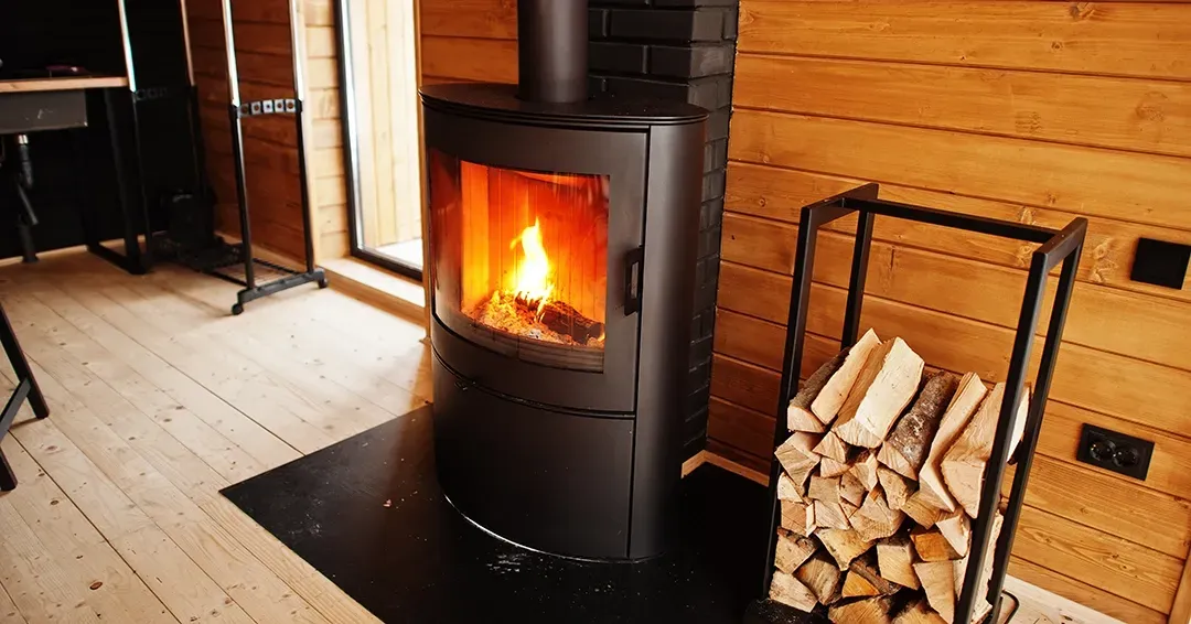 A wood stove is sitting in a wooden room next to a pile of logs.