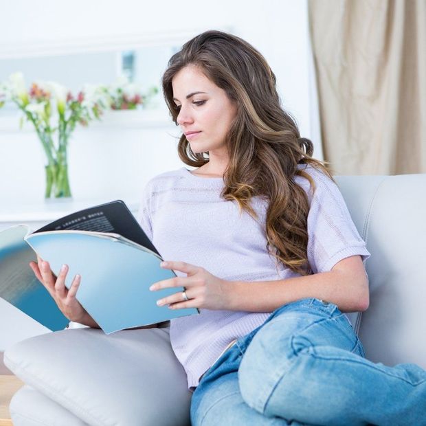 Woman reading a blue folder on a couch in a bright living room