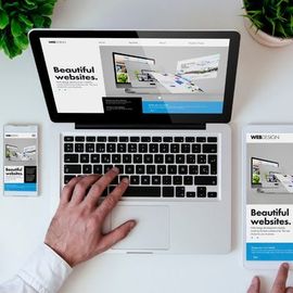 Overhead view of a laptop and smartphone showing responsive website mockups, with a hand on the keyboard.