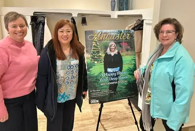 Three women stand beside a large poster on an easel in a bright room.
