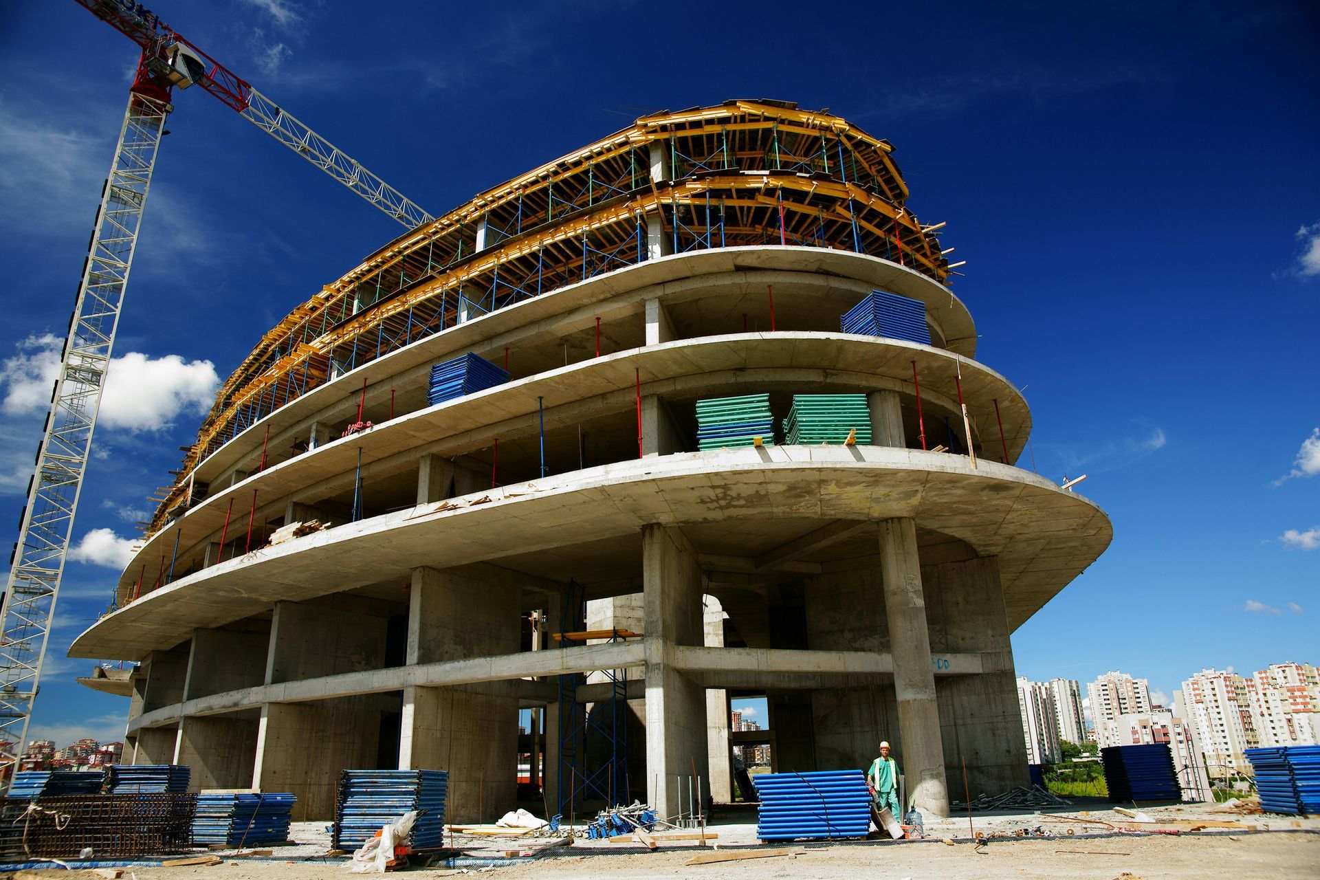 Building under construction with curved design, crane, and clear blue sky