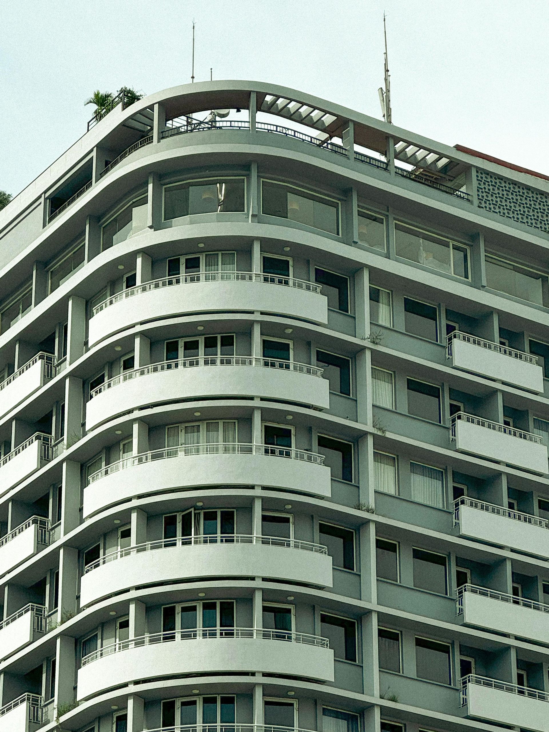 Curved corner of a multi-story gray building with balconies and windows, possibly an apartment.