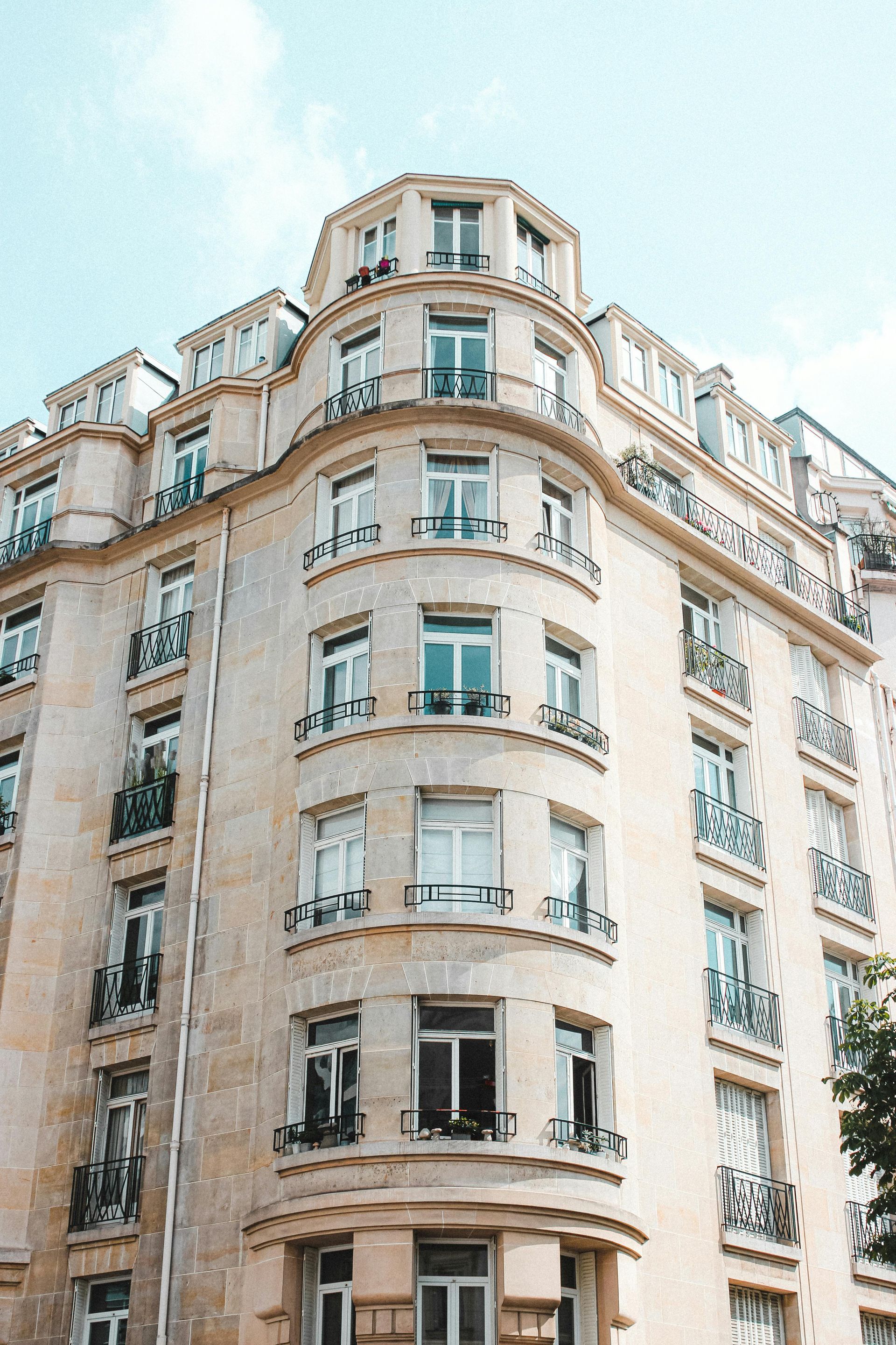 Beige Parisian building with balconies and windows against a light blue sky.