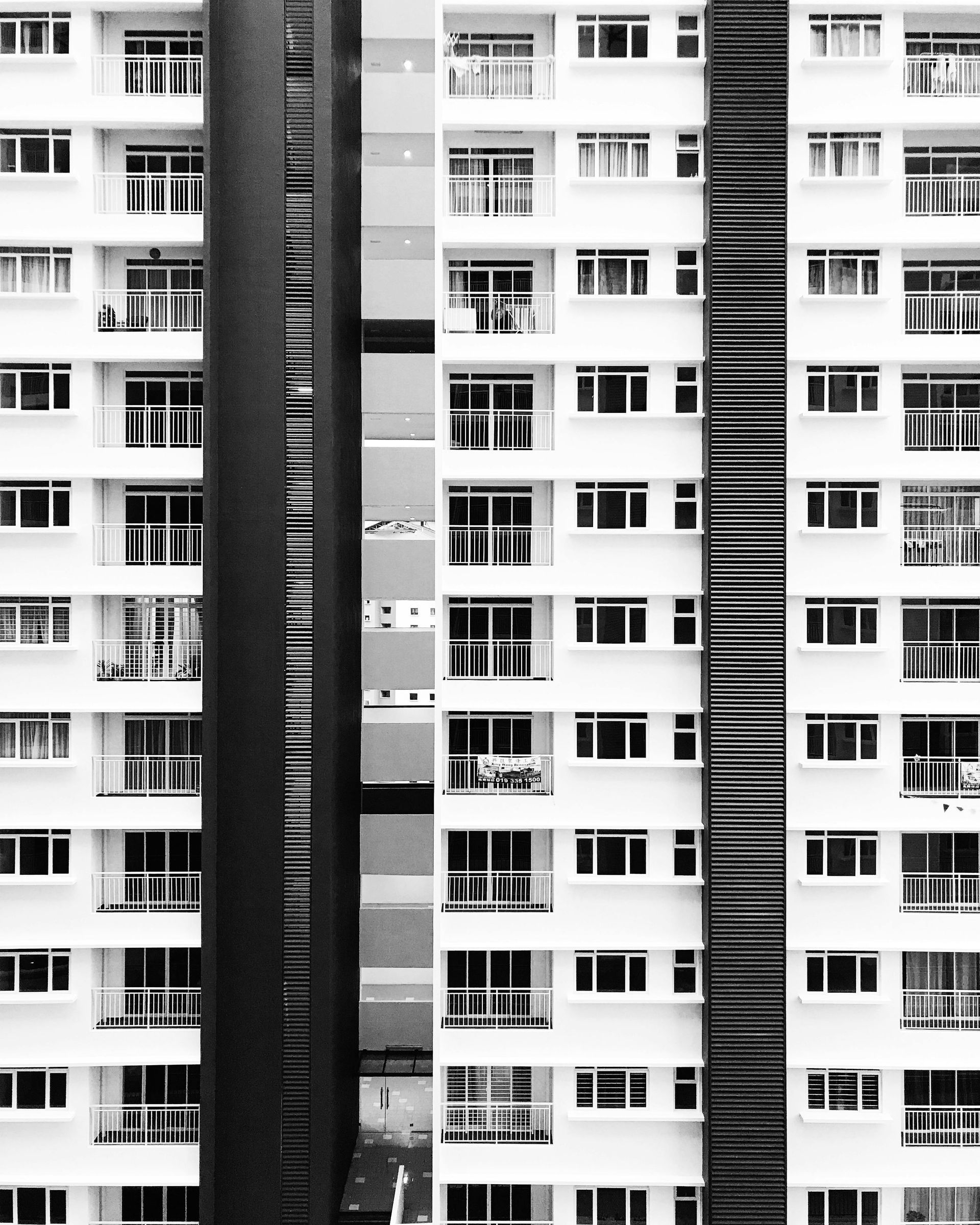 Black and white photo of a tall apartment building with many windows and balconies.