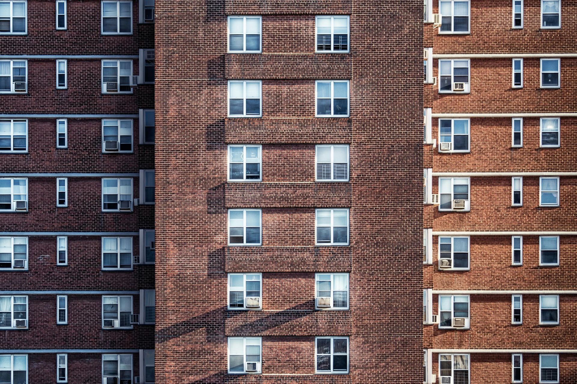 Brick apartment building with many windows, in a repeating pattern, catching the sunlight.