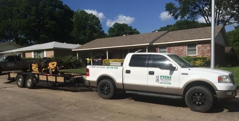 A white pickup truck with brown trim towing a flatbed trailer with machinery, parked on a residential street.