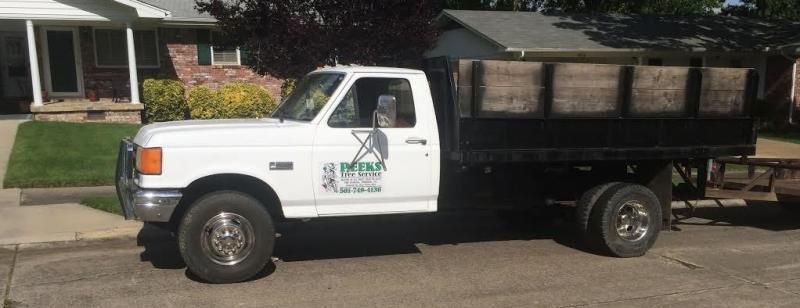 A white Ford flatbed truck with a company logo parked on a residential street in front of a house.