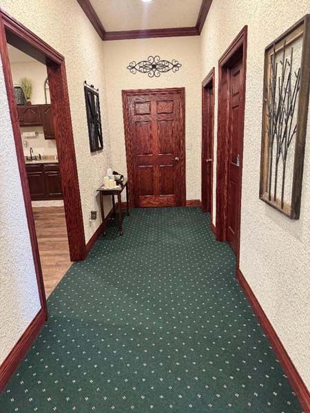 Long hallway with green carpet, wooden doors, and ornate decor on walls.
