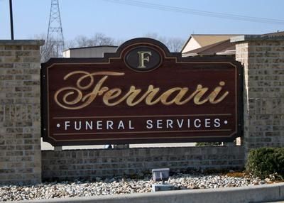 Sign for Ferrari Funeral Services: brown and gold lettering on a brick base.