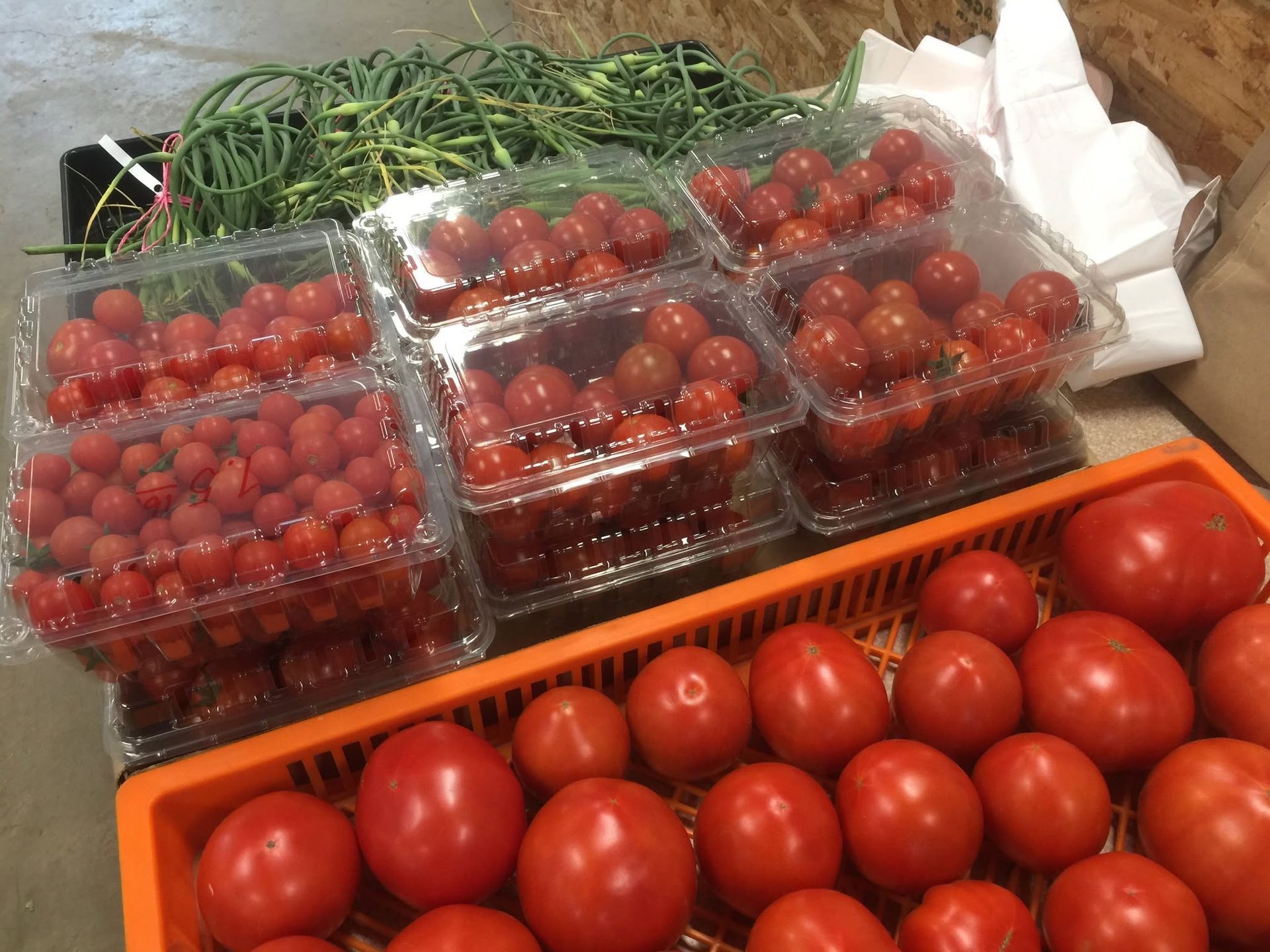 Clamshells of red cherry tomatoes and a crate of large red tomatoes on a market table