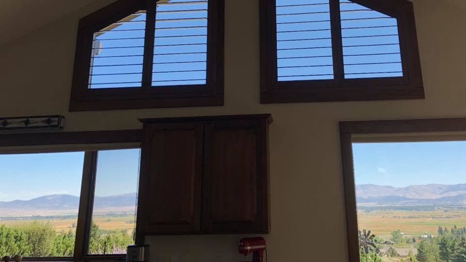 Interior view through a large window and open door to a bright landscape of fields and distant mountains.
