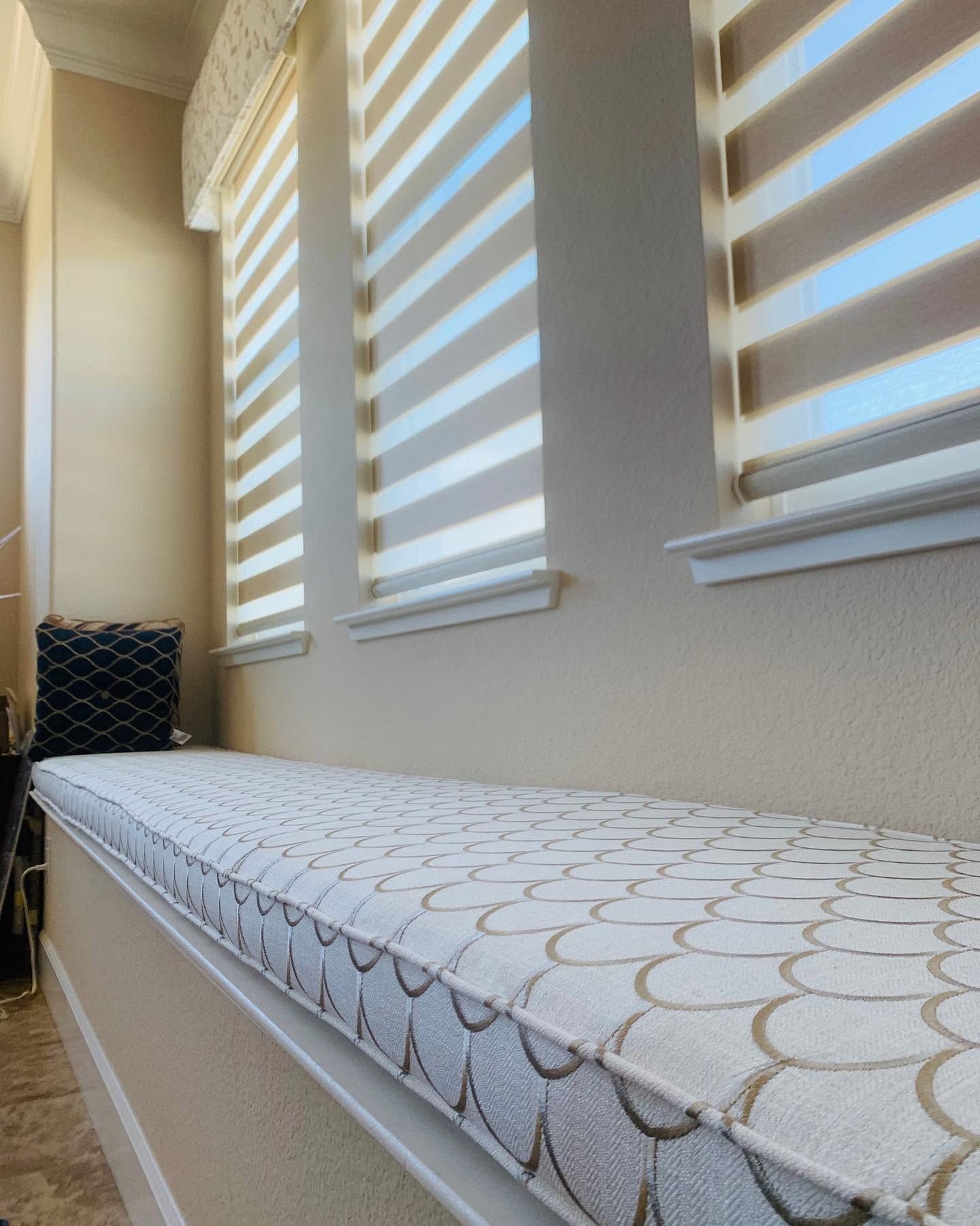Narrow upholstered bench by a window with striped blinds, in a bright hallway.