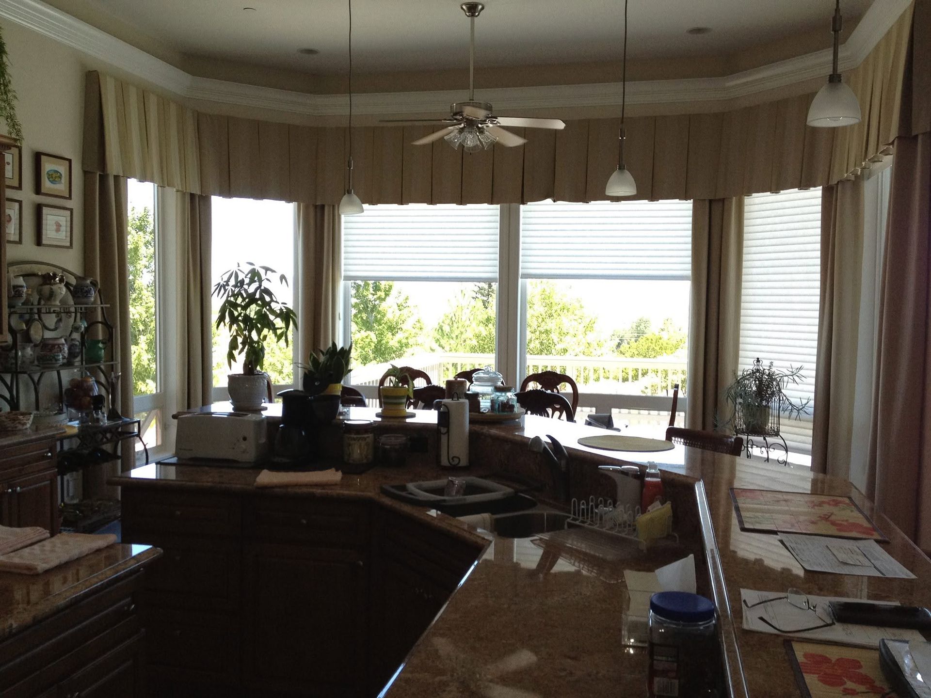 Bright kitchen and dining area with large windows, countertops, and a ceiling fan overlooking greenery