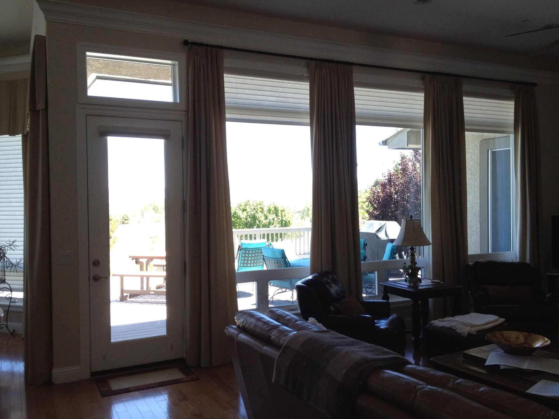 Living room with tall windows and sliding door opening to a sunny patio with pool and patio furniture