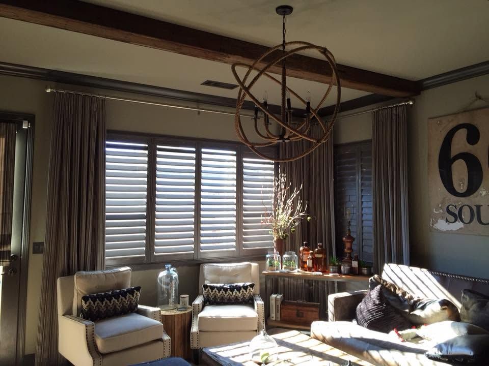 Modern living room with beige chairs, large window shades, and a hanging geometric light fixture