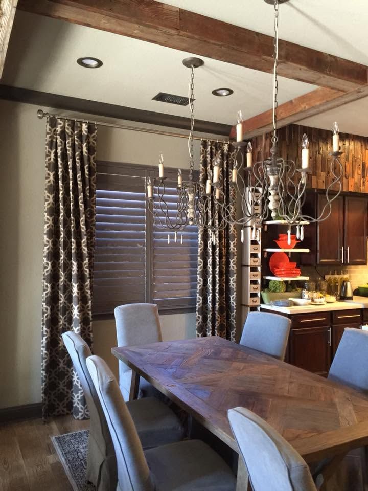 Modern dining room with wooden table, upholstered chairs, pendant lights, and a kitchen counter in the background