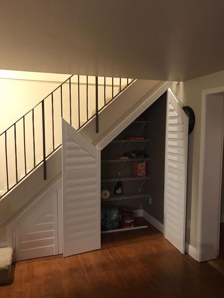 Under-stair pantry with open white doors revealing shelves and items in a home interior.