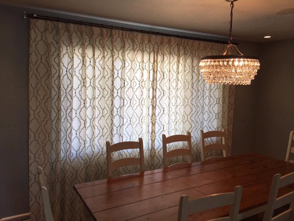 Dining room with wooden table, chairs, patterned curtains, and a hanging chandelier.