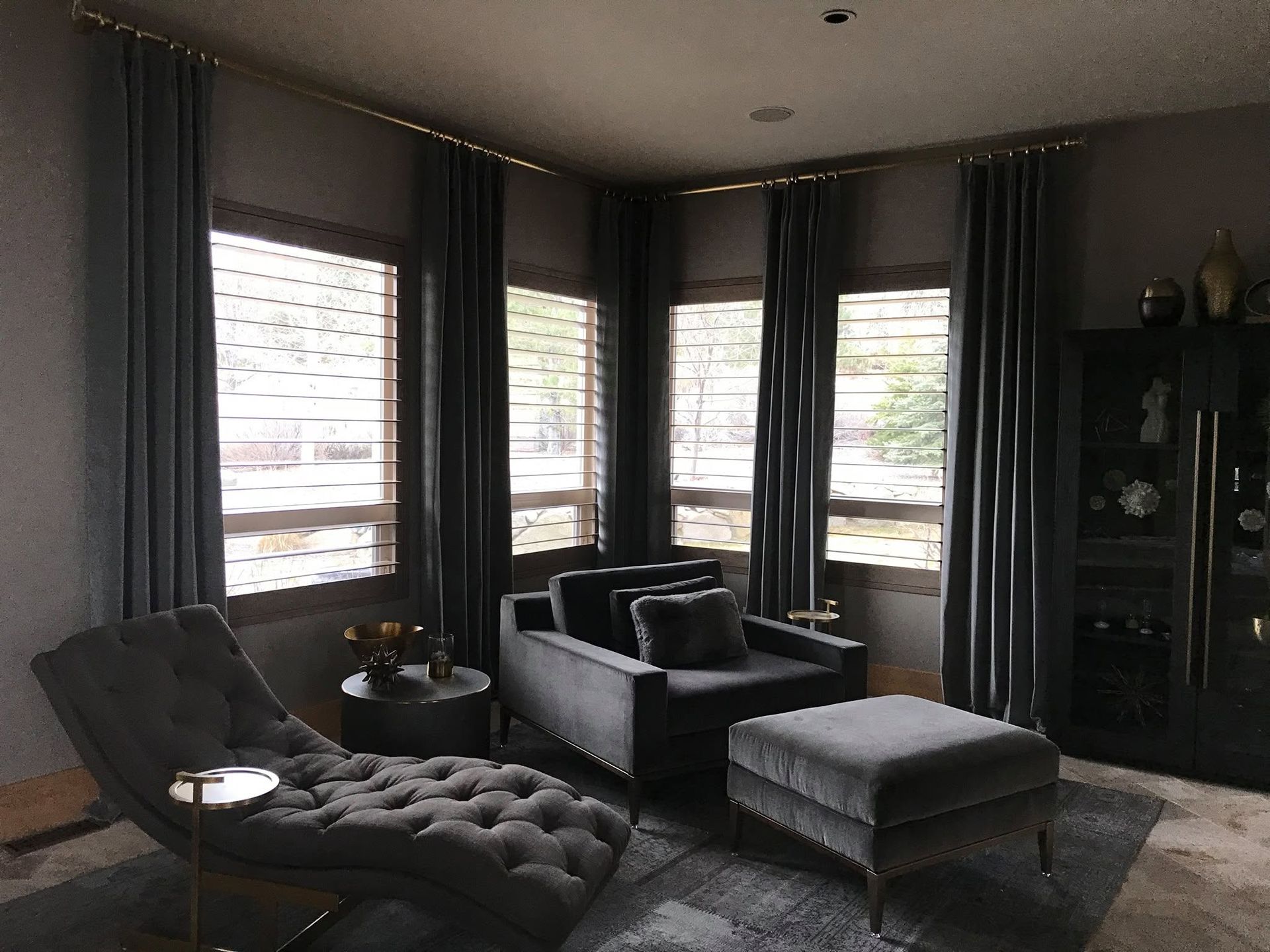 Modern living room with dark furniture, large windows, and a tufted chaise lounge.