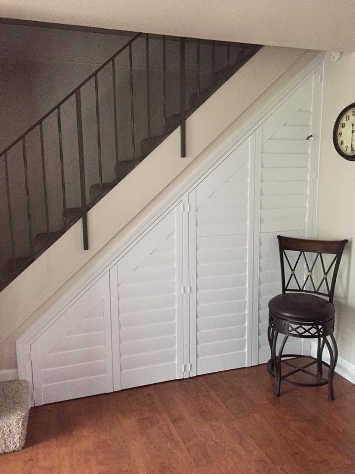 Staircase with black railing over white closet doors, wood floor, and a chair beside a wall clock