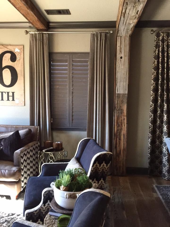 Cozy living room with blue patterned chairs, a window with curtains, and rustic wood beams