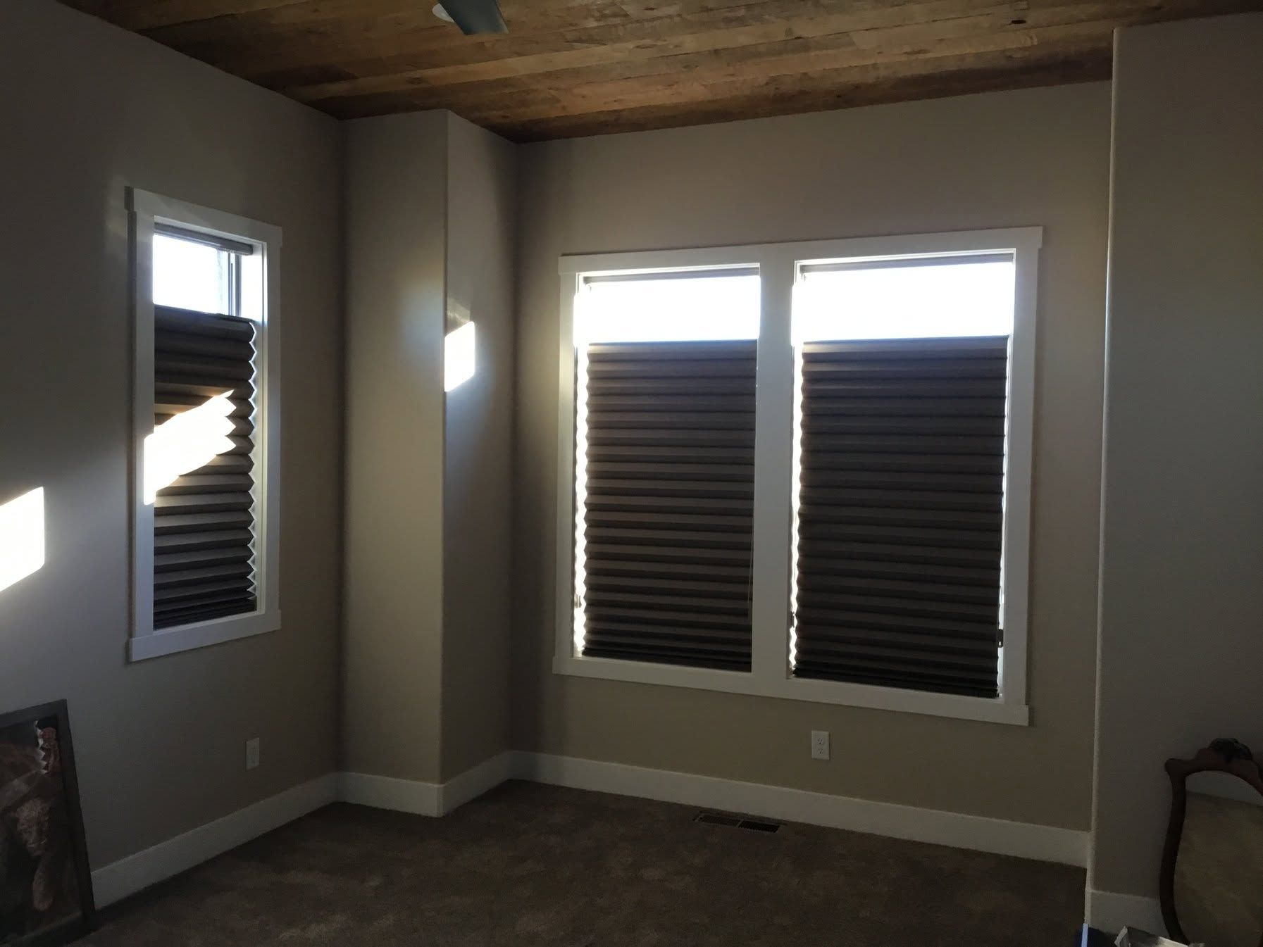 Empty room with gray walls, wood ceiling, and windows covered by blinds and sunlight.